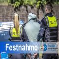 Polizistin und Polizist führen Mann in Handschellen zu einem Streifenwagen